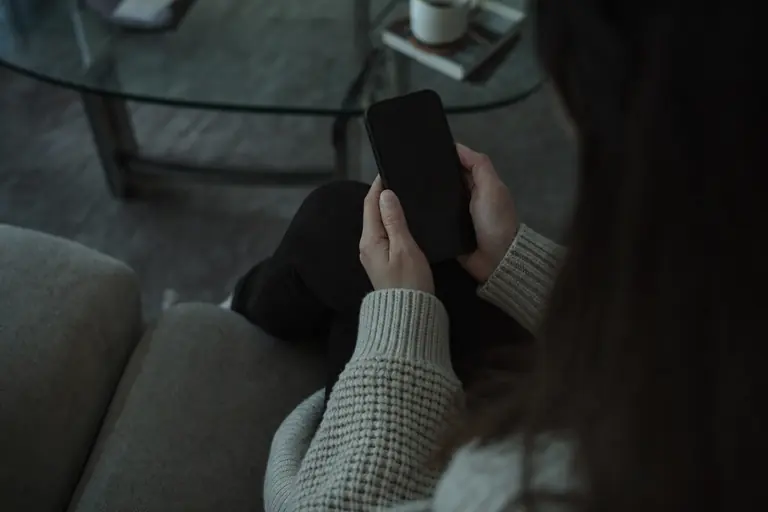 Handen die een smartphone vasthouden in een schemerige woonkamer