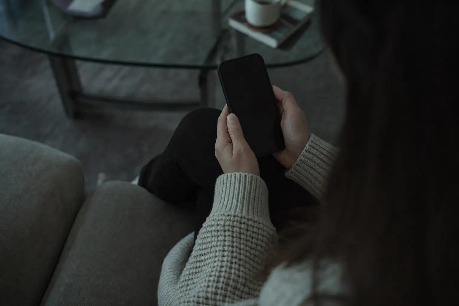 Handen die een smartphone vasthouden in een schemerige woonkamer